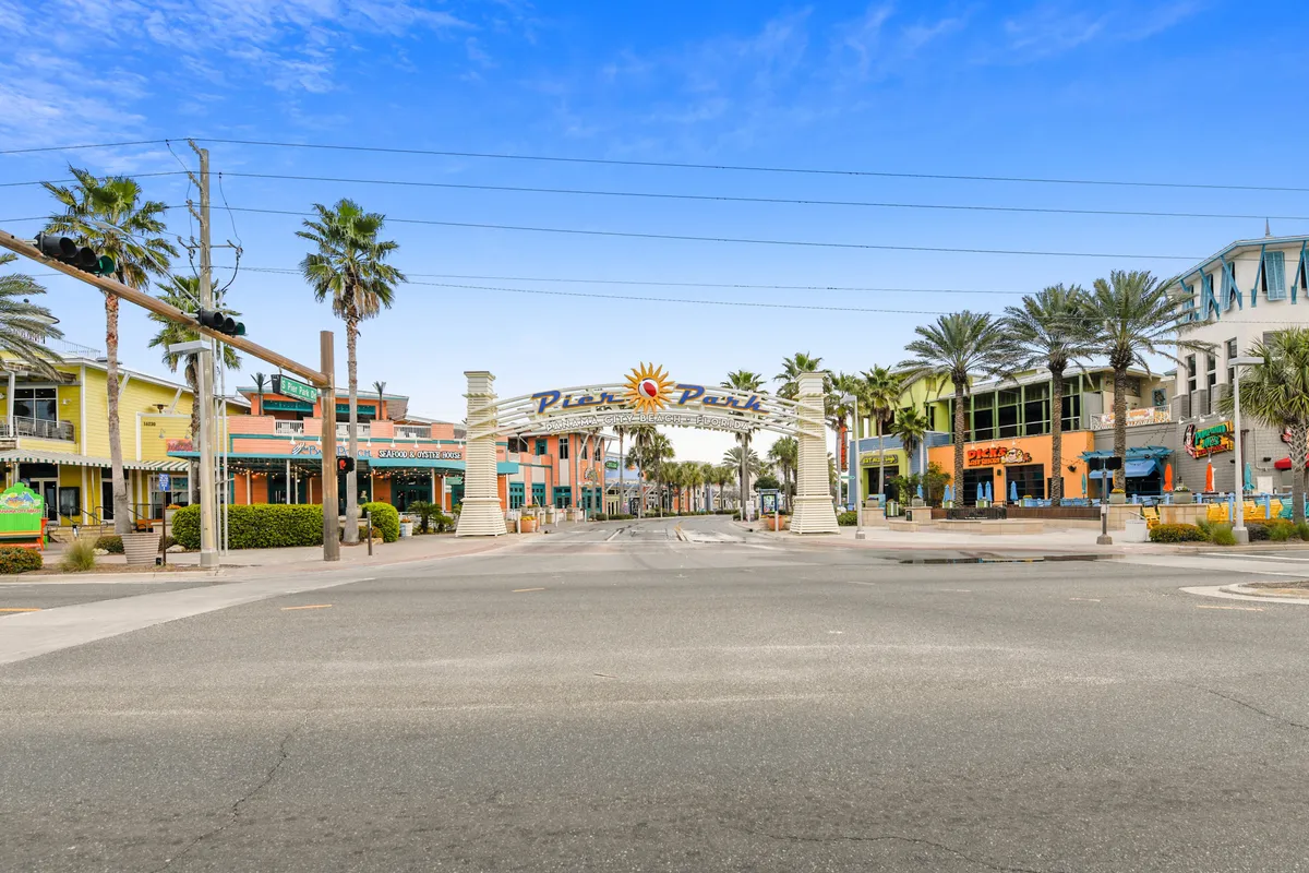 A lively and colorful outdoor area with a grand pavilion entrance archway, bustling storefronts, and swaying palm trees creates an energetic atmosphere perfect for shopping, dining, and exploring with family. The scene exudes local flavor and excitement.