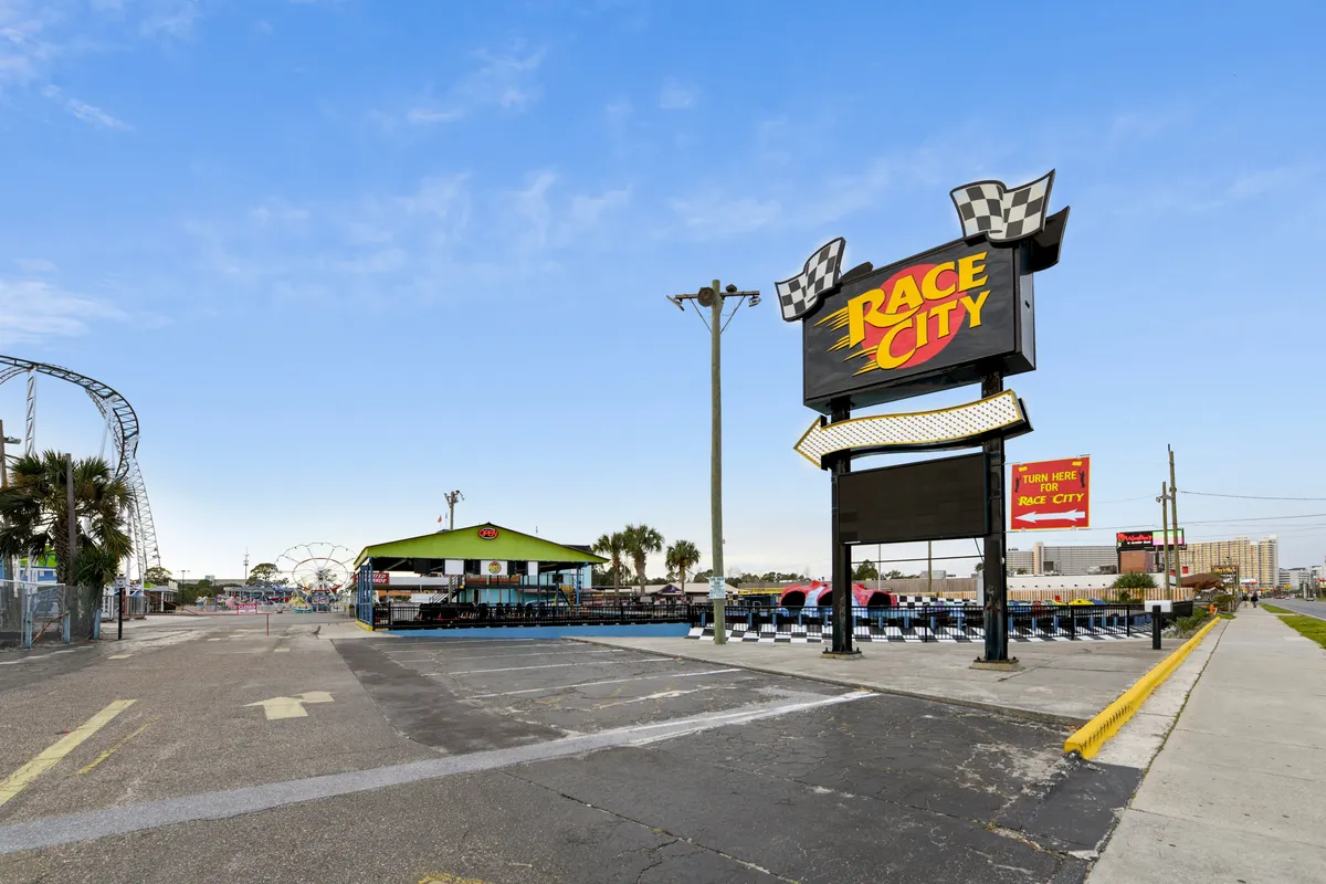 A vibrant exterior view of Race City features a large, colorful sign, a lively go-kart track, and carnival rides in the background, bustling with children and families enjoying the attractions.
