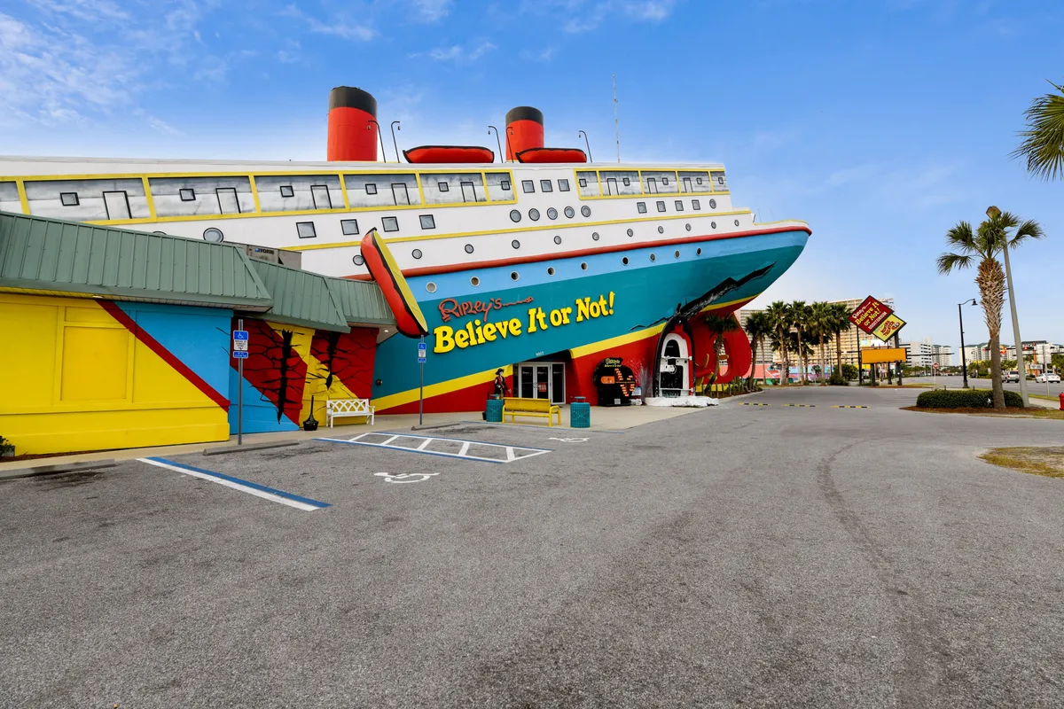 The bright, whimsical exterior of a local attraction, featuring a colorful ship structure and bold signage surrounded by vibrant palm trees. The scene suggests excitement and discovery, hinting at fun experiences like WonderWorks nearby.