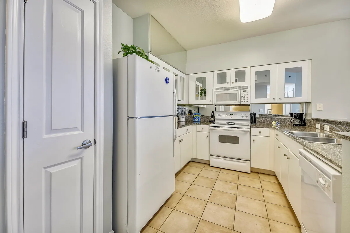 This image displays a clean, inviting kitchen featuring a white refrigerator, oven, ample countertop space, and a sink. The layout is practical and organized, offering a comfortable space for meal preparation and gatherings.