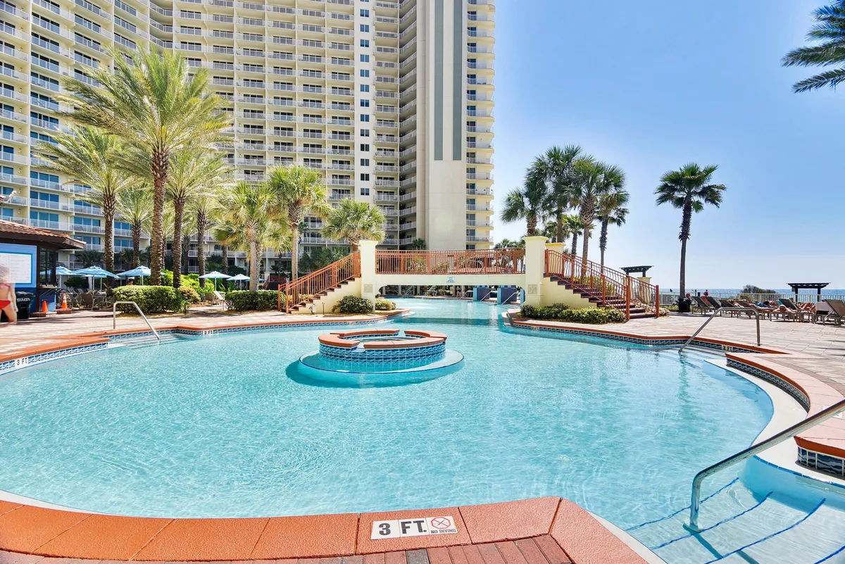 A stunning view of a resort-style pool area, complete with a large swimming pool, hot tub, surrounding palm trees, deck chairs, and the building facade in the background. The scene is vibrant, luxurious, and designed for relaxation or social gatherings.