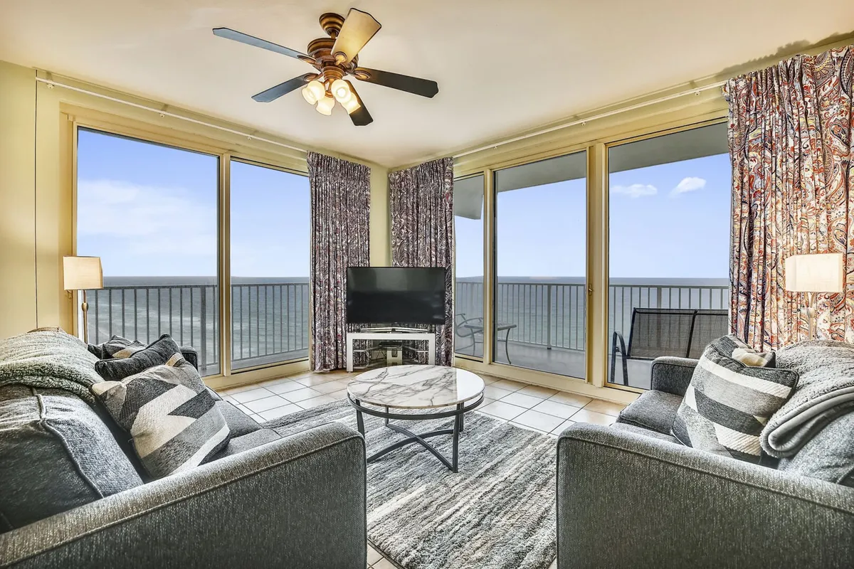 An inviting living room with expansive windows overlooking the ocean, comfortable sofas arranged for socializing, decorative curtains, and a central coffee table. The ambiance is warm and welcoming, ideal for enjoying the coastal setting.