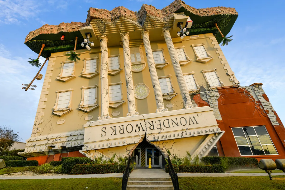 An eye-catching, upside-down building with ornate columns and the bold 'WONDERWORKS' sign dominates the scene. The structure appears playful and whimsical, hinting at the interactive, educational exhibits inside. Its unusual architecture draws attention and promises a unique family attraction experience.